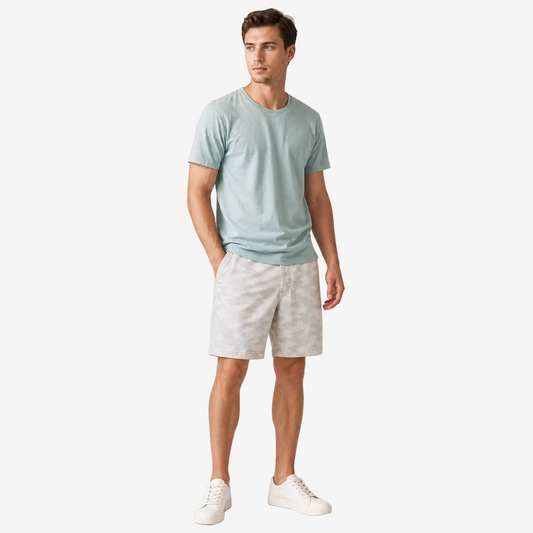 A man modeling a light sage green crewneck t-shirt and light gray patterned shorts against a plain white studio background.