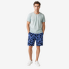 A man modeling a light sage green crewneck t-shirt and blue camouflage shorts against a plain light gray studio background.