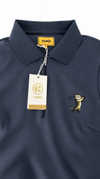 A close-up of a navy blue polo shirt with a yellow TIGRÉE neck label, a white hangtag, and a yellow embroidered tiger mascot on the chest.
