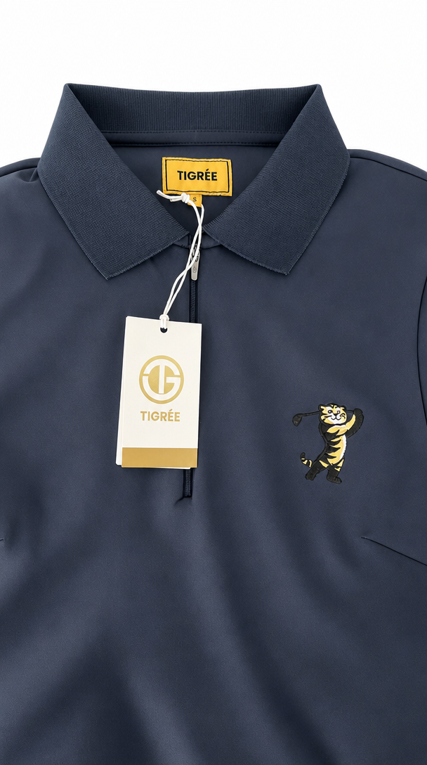 A close-up of a navy blue polo shirt with a yellow TIGRÉE neck label, a white hangtag, and a yellow embroidered tiger mascot on the chest.