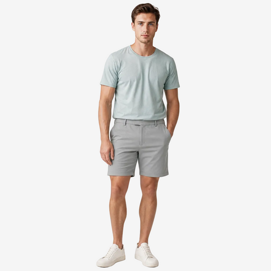A man modeling a light sage green crewneck t-shirt and light gray shorts against a plain light gray studio background.