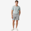 A man modeling a light sage green crewneck t-shirt and light gray shorts against a plain light gray studio background.