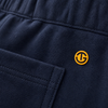 Close-up of navy blue ribbed fabric with a small yellow circular logo patch on the side and a stitched pocket.
