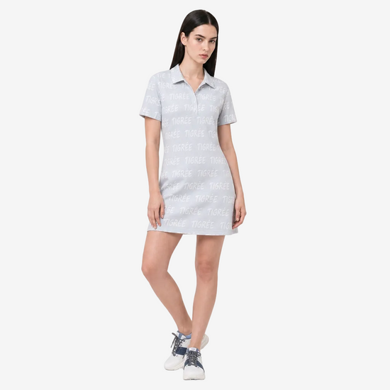 A woman modeling a light blue short-sleeve polo shirt dress with a white repeating text pattern, paired with white sneakers, against a plain light gray studio background.