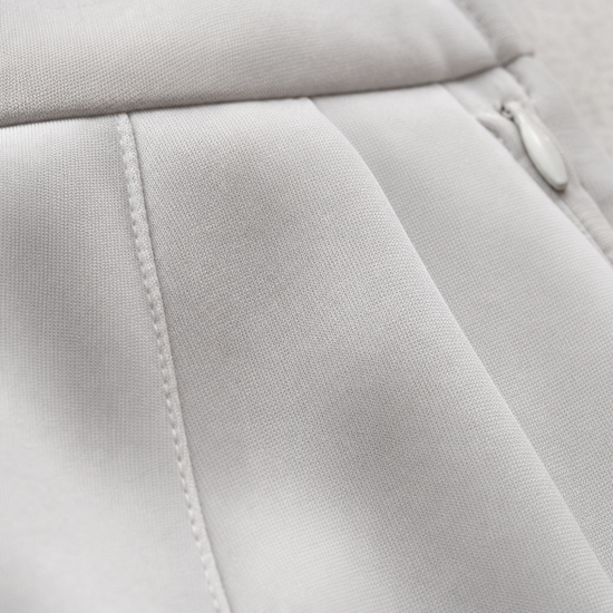 Close-up of a light gray fabric surface with stitched paneling and a small zipper pull visible on the right side.