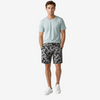 A man modeling a light blue crewneck t-shirt and gray/black camouflage shorts with white sneakers, standing against a plain light gray studio background.