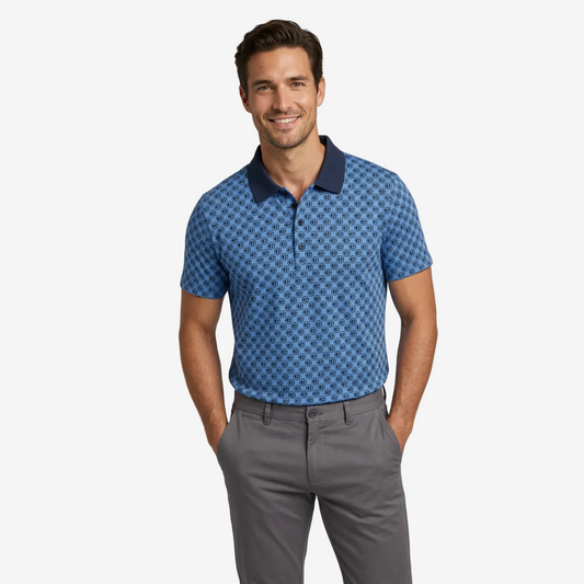 A man wearing a blue short-sleeve polo shirt with a geometric pattern and a dark navy collar, paired with gray trousers, standing against a light gray studio background.