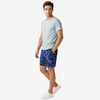 A man modeling a light sage green crewneck t-shirt and blue camouflage shorts, paired with white sneakers, against a plain light gray studio background.
