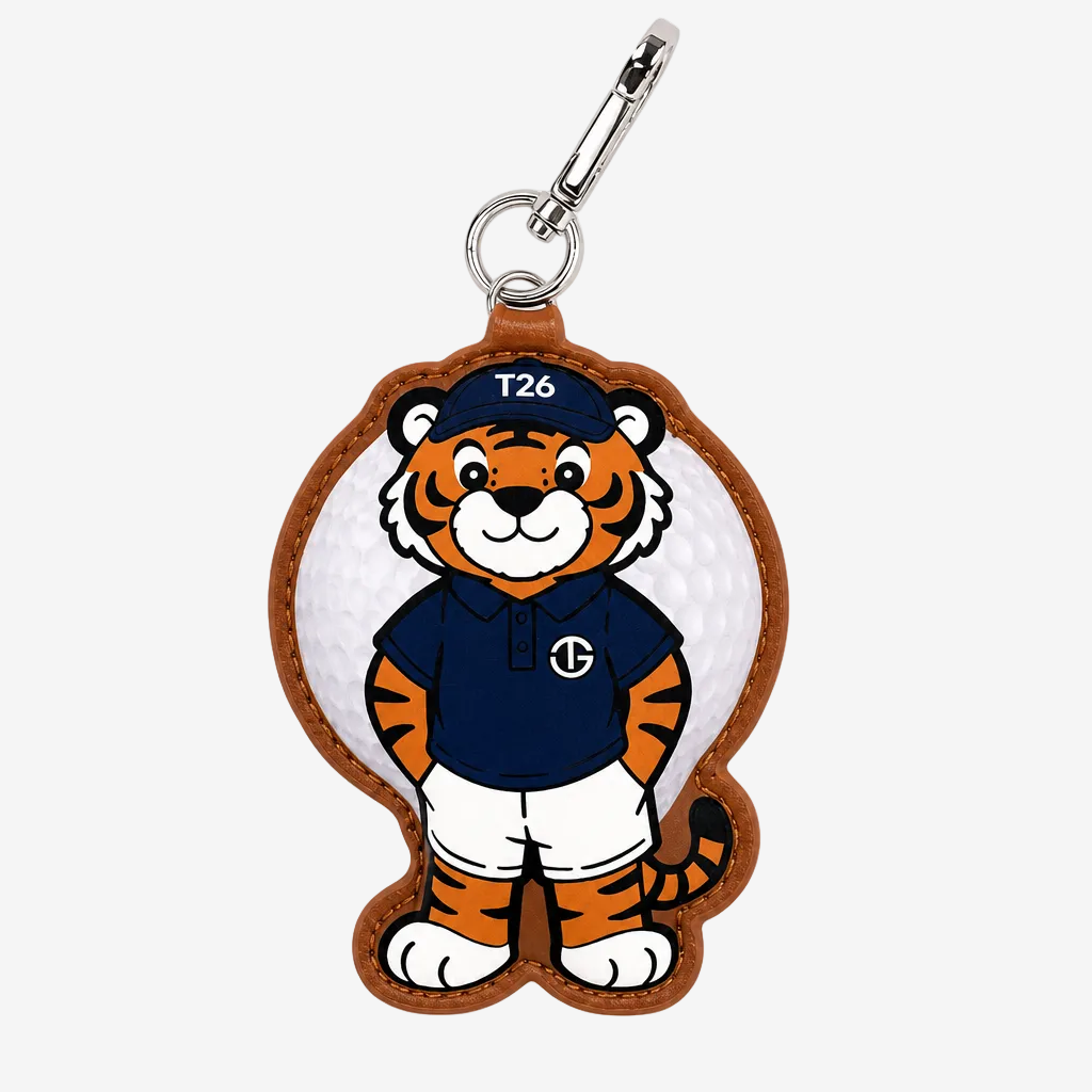 A golf keychain featuring a cartoon tiger mascot in a navy blue polo shirt and white shorts, attached to a white golf ball with a brown leather border and silver carabiner clasp.