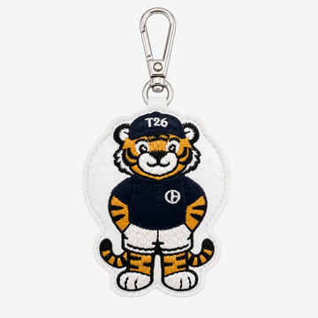 An embroidered tiger mascot keychain or bag charm on a white background. The character wears a navy blue jersey with a white 'H' logo, white shorts, and a navy cap with 'T26' in white.