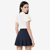 A model is shown from the back wearing a white short-sleeve polo shirt with a small yellow circular logo on the left sleeve, paired with a dark navy pleated mini skirt, against a light gray studio background.