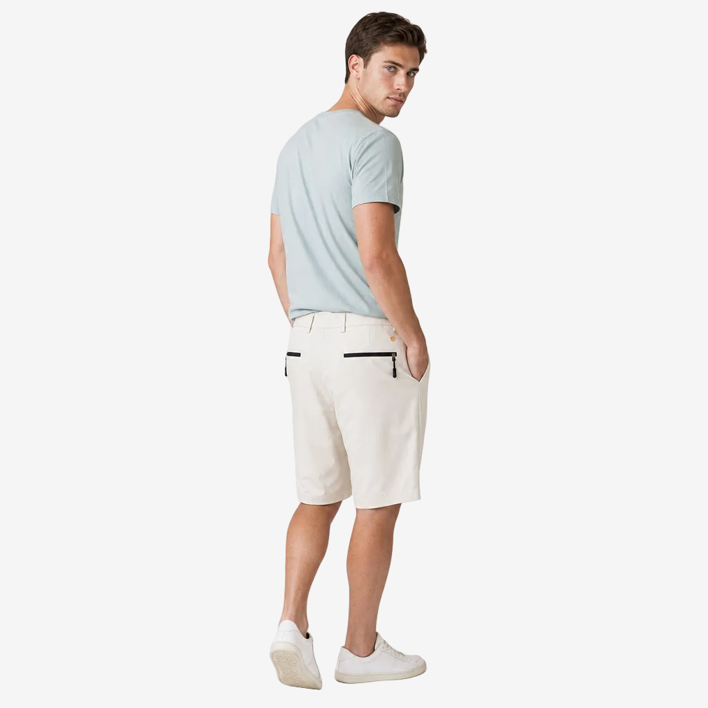 A man wearing a light blue t-shirt, off-white shorts with black zipper details, and white sneakers, photographed from the back against a plain light gray studio background.