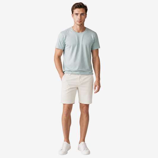 A man modeling a light blue crew-neck t-shirt and off-white shorts against a plain light gray studio background.
