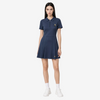 A woman modeling a navy blue short-sleeve polo dress with a small gold embroidered logo on the chest, paired with white socks and white sneakers, against a light gray studio background.
