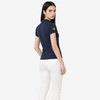 A woman modeling a navy blue short-sleeve polo shirt with a gold embroidered logo on the sleeve, paired with white pants, photographed against a light gray studio background.