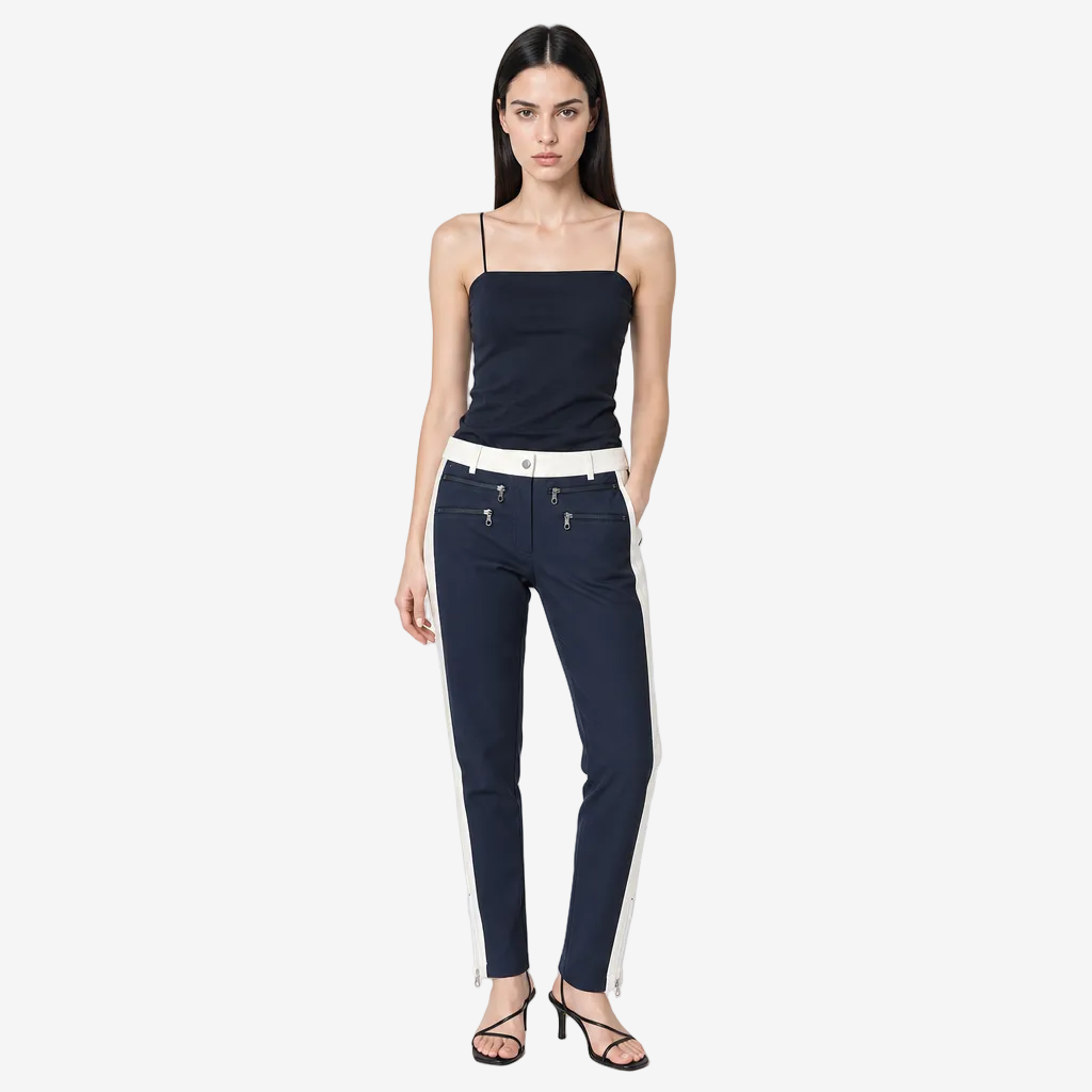 A model stands against a light gray studio background wearing navy blue skinny jeans with a contrasting white side stripe and white waistband, paired with a navy camisole and black strappy heels.