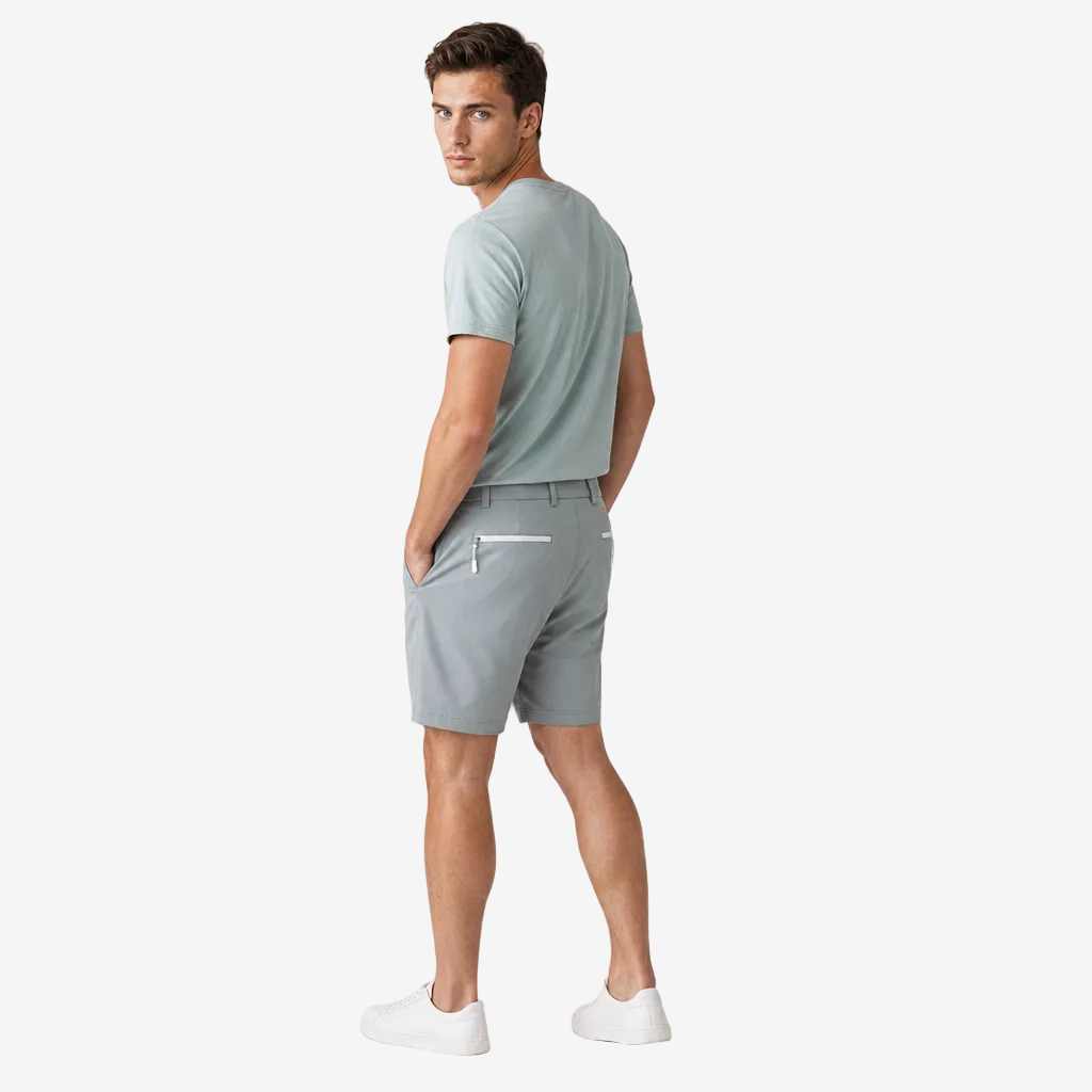 A man wearing a light sage green t-shirt and matching light sage green shorts, shown from a side-back angle against a plain light gray studio background.