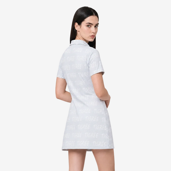 A woman modeling a short-sleeve collared dress from the back, featuring an allover light gray 'TIGREES' text pattern on a white base, set against a plain light gray studio background.