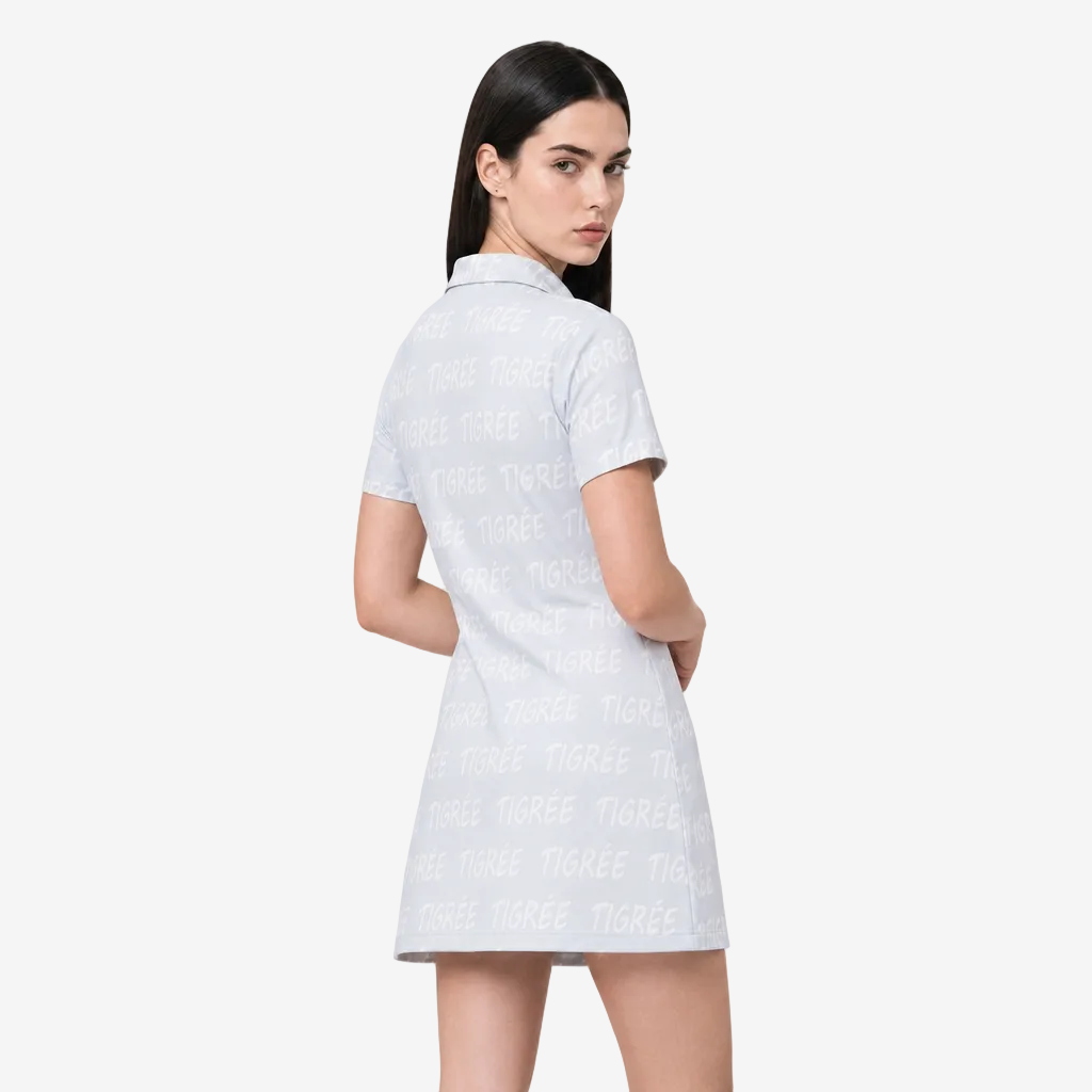 A woman modeling a short-sleeve collared dress from the back, featuring an allover light gray 'TIGREES' text pattern on a white base, set against a plain light gray studio background.