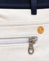 Close-up of a white zippered pocket on a golf jacket, featuring a silver zipper pull with a G-100 logo and a small gold circular G-100 emblem on the front.