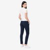 A woman is shown from the back wearing a white short-sleeve polo shirt with a gold circular patch on the sleeve, navy blue slim-fit trousers, and white sneakers, set against a plain light gray studio background.