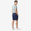 A man wearing navy blue shorts with a distinctive orange accent line on the back pocket, paired with a light sage green t-shirt and white sneakers, photographed from the back against a neutral studio background.