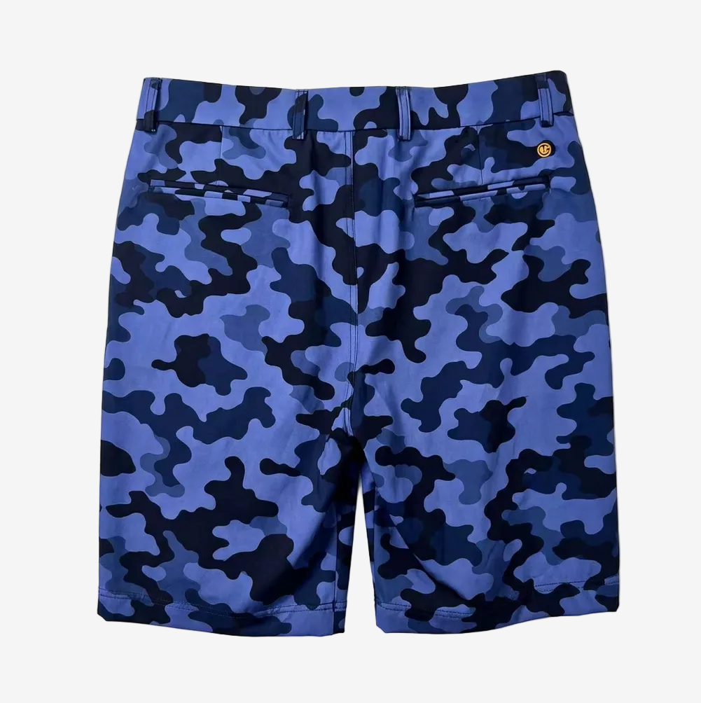 Blue and navy camouflage shorts with a small gold circular logo on the right hip, shown flat against a light gray background.