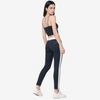 A woman modeling a pair of dark navy skinny pants with a white side stripe, paired with a matching navy crop top and white sneakers, photographed against a light gray studio background.