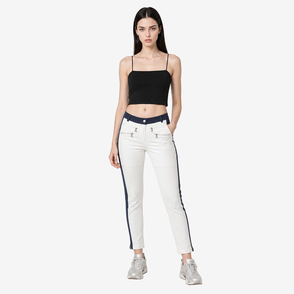 A model stands against a light gray studio background wearing white skinny jeans with navy blue side stripes, a black crop top, and silver sneakers.