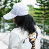 Person wearing a white cap and a white hoodie with a tiger design outdoors.