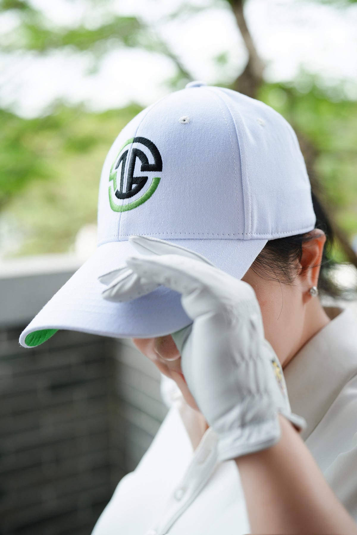Person wearing a white cap with a logo and a golf glove, outdoors.