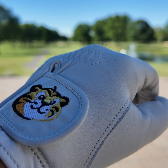 White golf glove with a tiger logo on a blurred outdoor background