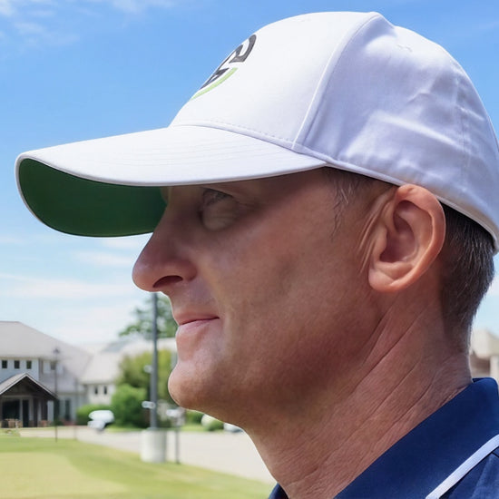 Man wearing a white cap with a logo on a golf course