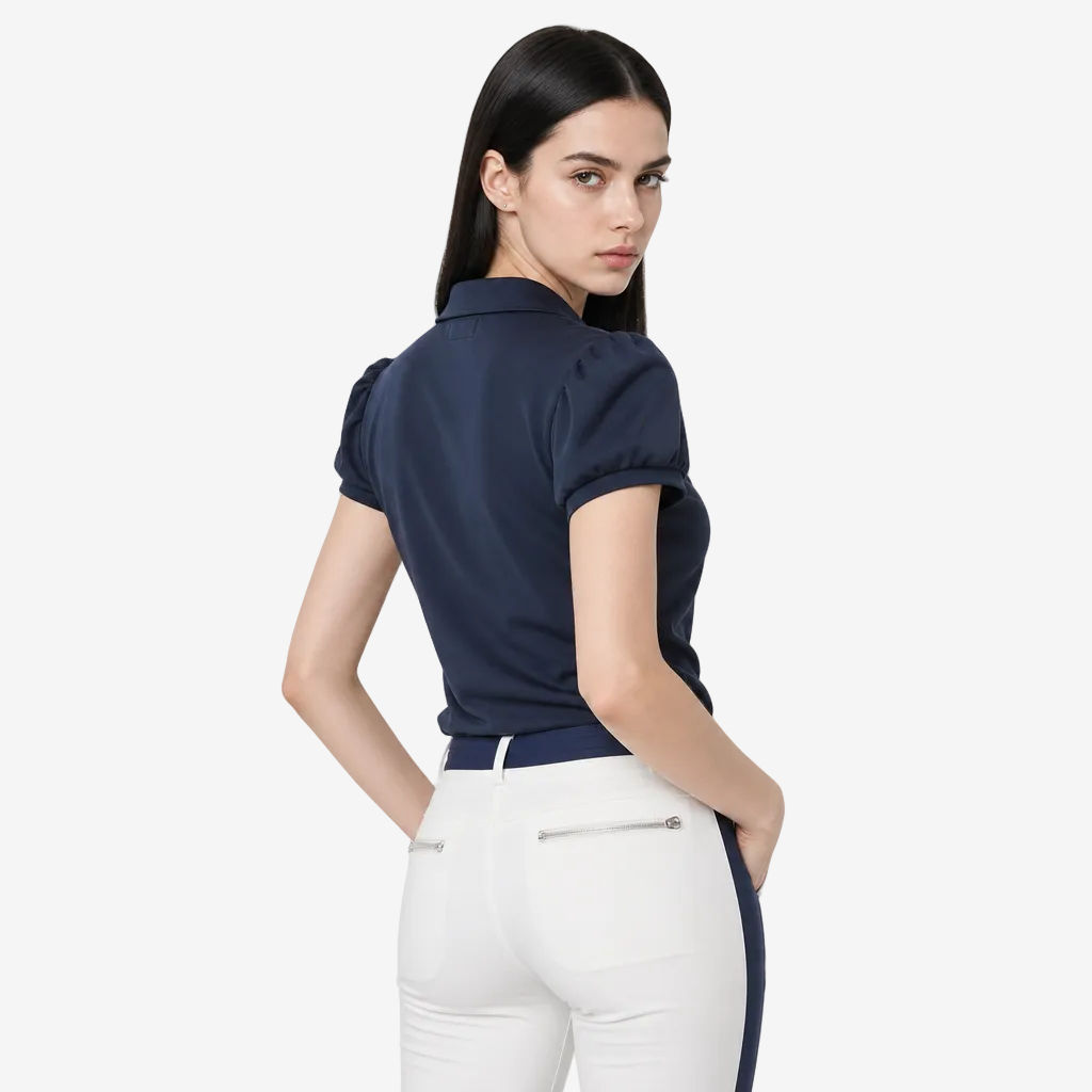 A woman modeling a navy blue short-sleeve polo shirt with a yellow circular logo on the sleeve, paired with white pants, photographed against a light gray studio background.