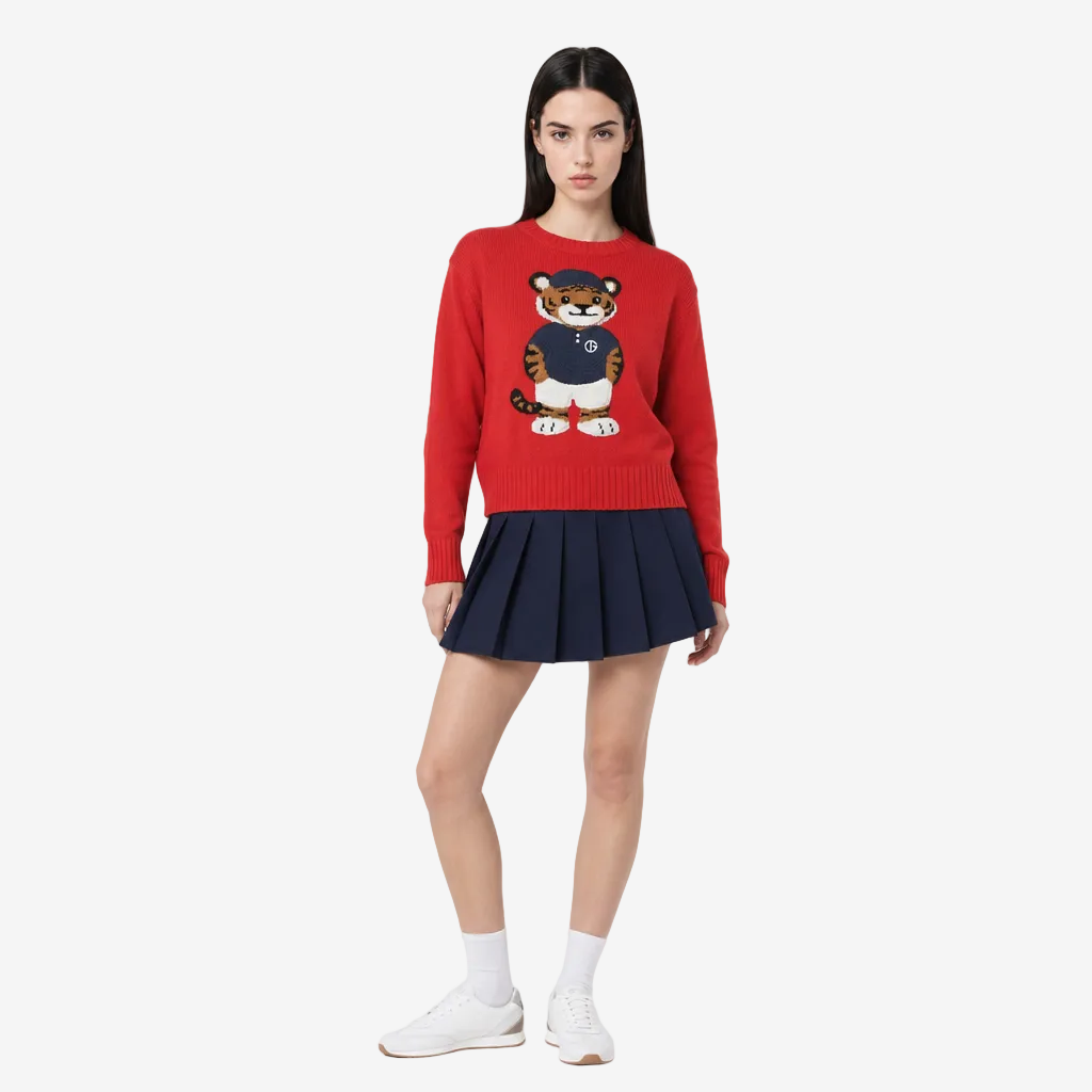 Woman wearing a red sweater with a tiger design and a navy pleated skirt on a white background