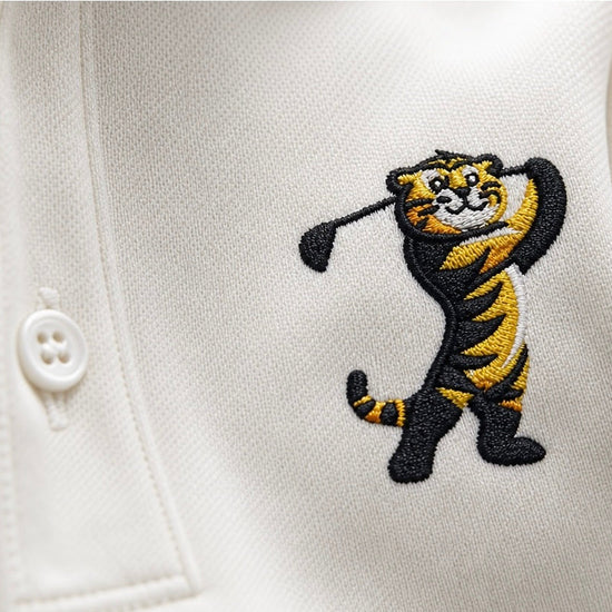 Close-up of a white polo shirt featuring an embroidered tiger mascot holding a golf club on the chest.