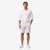A man modeling a white long-sleeve linen shirt and white patterned shorts against a light gray studio background.