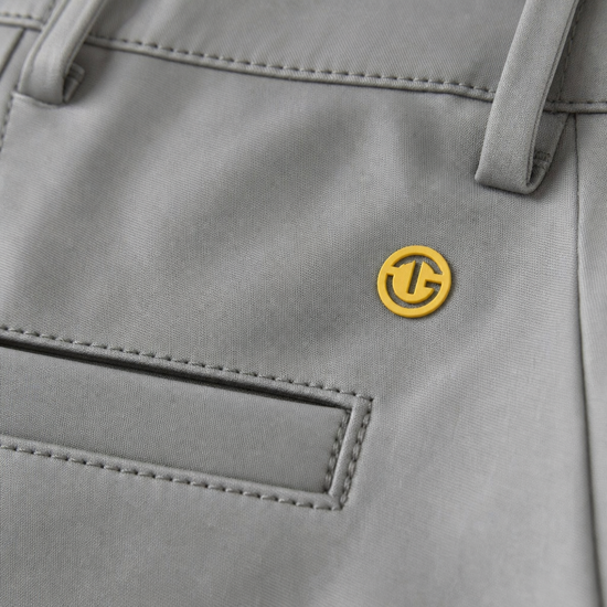 Close-up of a light gray fabric garment, likely a jacket or coat, showing a small circular yellow logo patch with a stylized 'G' on the chest.