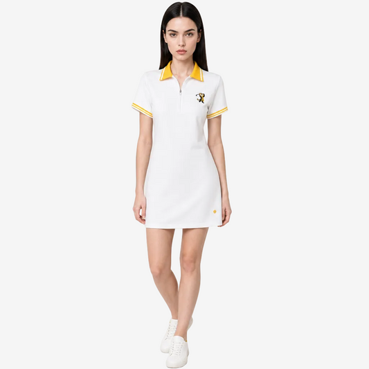 A woman modeling a white short-sleeve polo dress with yellow collar and sleeve trim, featuring a small embroidered logo on the left chest, set against a plain light gray studio background.