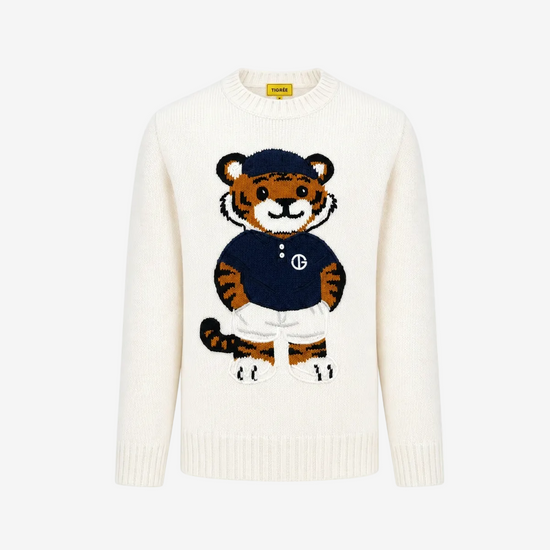 An off-white knit crewneck sweater featuring a large embroidered cartoon tiger mascot wearing a navy blue shirt and white trousers on the front. The brand label on the inner collar reads 'SWEAT'.