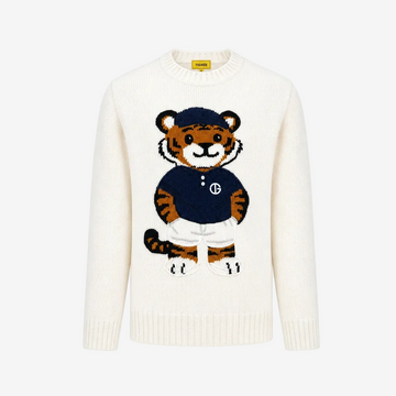 An off-white knit crewneck sweater featuring a large embroidered cartoon tiger mascot wearing a navy blue shirt and white trousers on the front. The brand label on the inner collar reads 'SWEAT'.