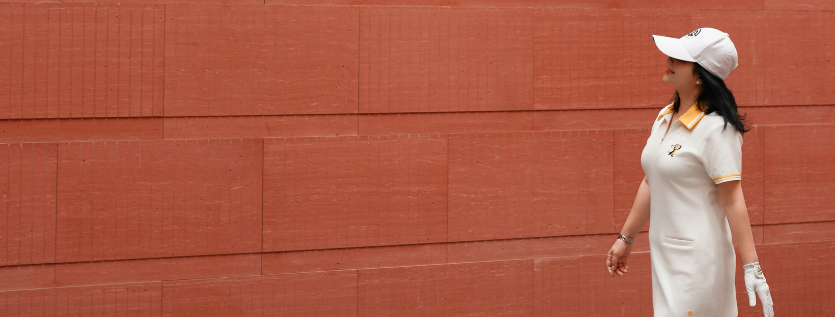 Woman in a white outfit and cap standing against a red brick wall